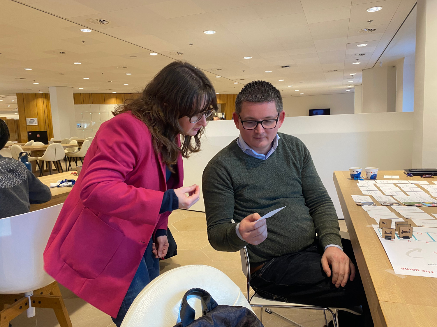 Un participant à l'atelier et Daphné (l'une des formatrices) regardent intensément une carte à jouer lors d'une session du jeu de société.