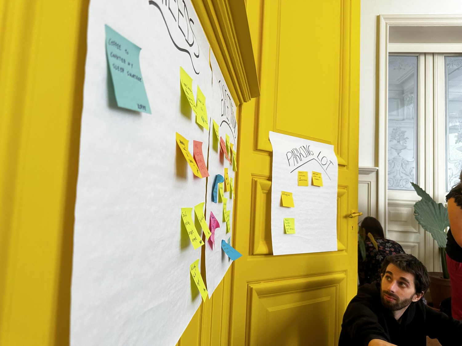 Jan de Eleven Ways regarde un tableau blanc sur lequel sont collées des notes. Les mots « besoins », « attentes » et « place de parking » sont visibles.